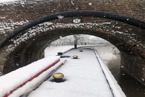 canal boat in the snow going under a bridge